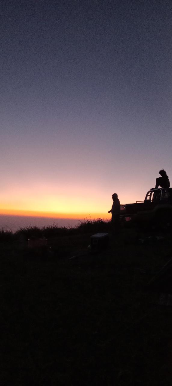 Two men seated on a jeep watching the sunrise from a mountain top in Sri Lanka 